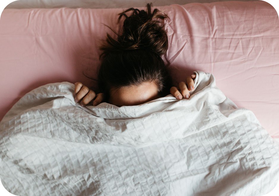 Woman hiding in bed concerned about the color of her vaginal discharge.