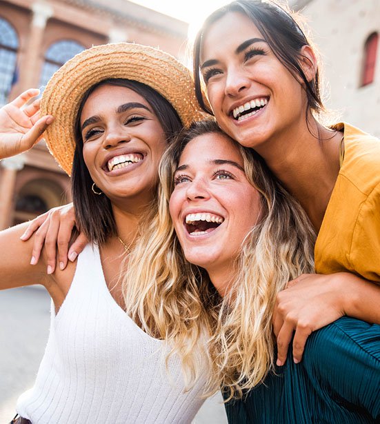 Three young multiracial women laughing and walking together on a city street outdoors.