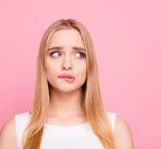 Portrait of a young woman making a nervous expression, against a plain background.